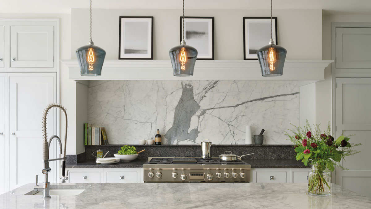 A trio of grey hand-blown glass pendant lights over a kitchen island designed by british kitchen makers Martin Moore.